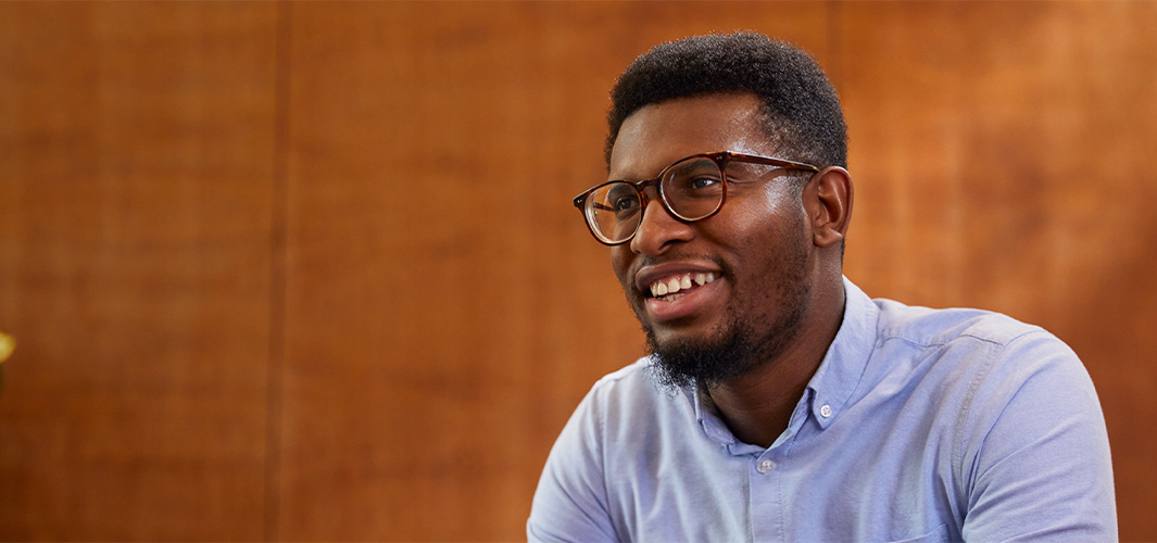 Chidi sedí, usmívá se a dívá se mimo objektiv.