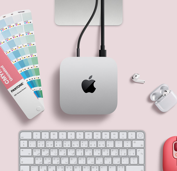 لقطة علوية لجهاز Mac&nbsp;mini فضي اللون ضمن إعداد مكتبي مع سماعات AirPods ولوحة مفاتيح لاسلكية وردية اللون وماوس لاسلكي وردي وعينات ألوان على شكل مروحة
