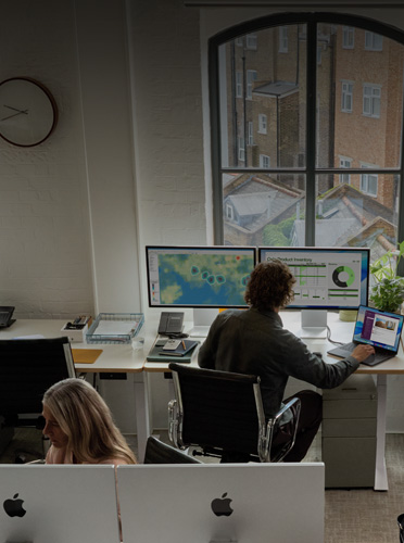 Employees sit in an office, each with a multiple screen setup that includes two Studio Display devices and a MacBook Neo
