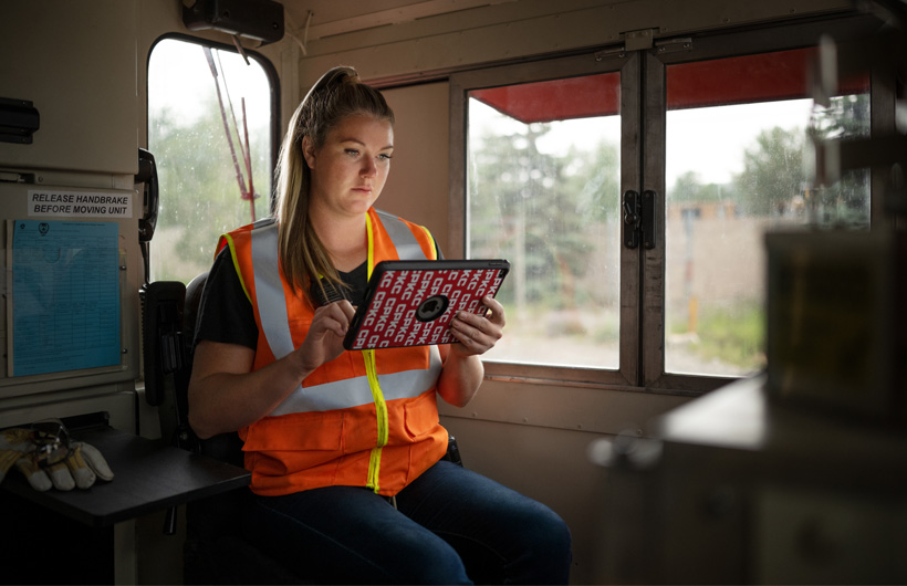Trabalhadora ferroviária sentada numa carruagem de comboio a olhar para o iPad