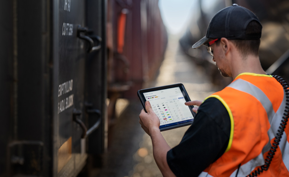 Trabalhador ferroviário junto a um comboio a verificar um iPad que apresenta informações de horários