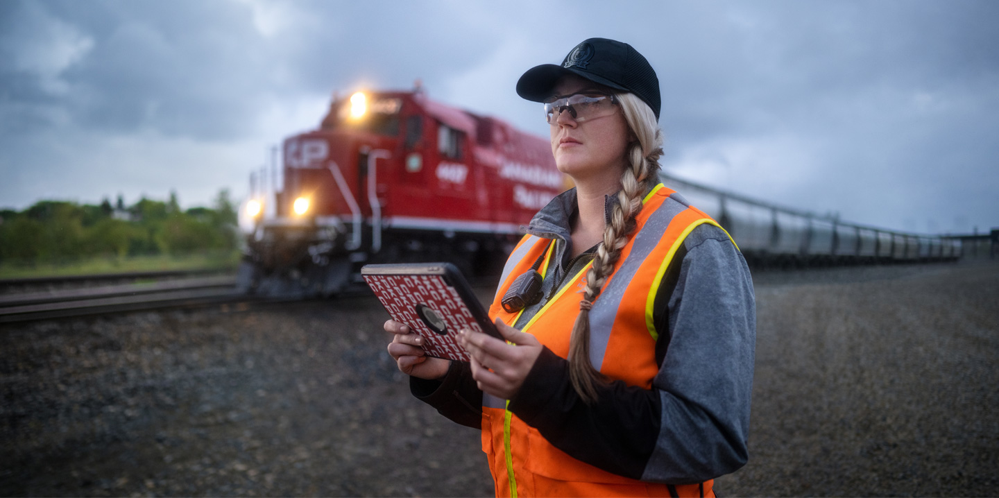 Trabalhadora ferroviária segura um iPad e verifica os carris enquanto passa um comboio
