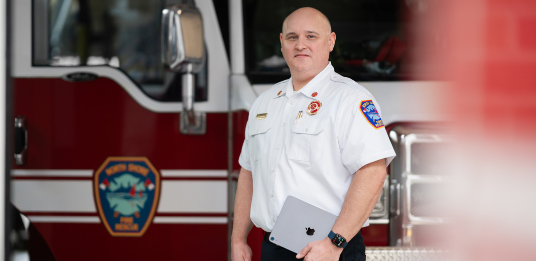 Le chef des pompiers se tient devant un camion de pompiers avec un iPad à la main et une Apple Watch au poignet